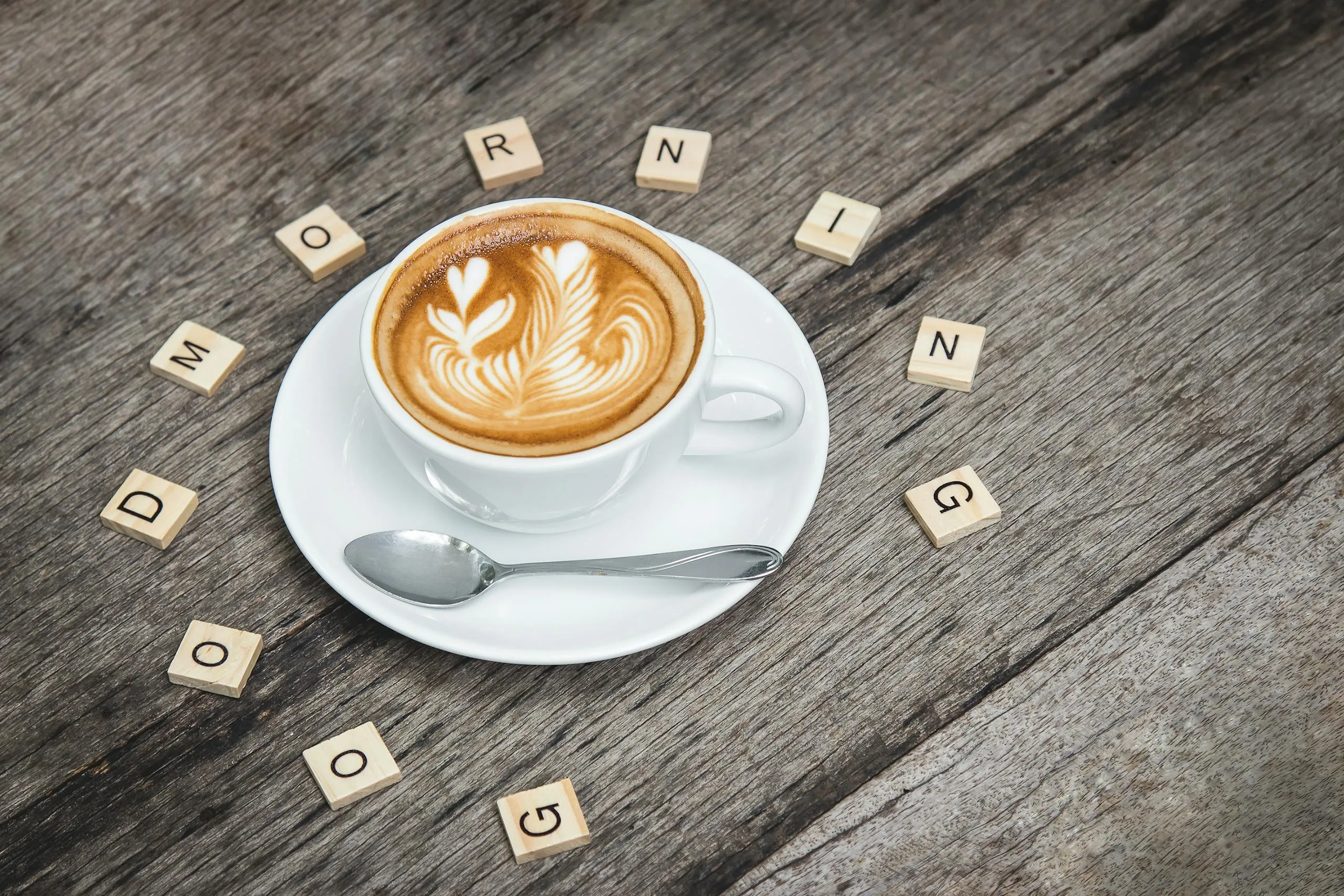 My Daily Routine for Freelancers: Cup of cappuccino with latte art surrounded by Scrabble letters spelling 'Good Morning'.